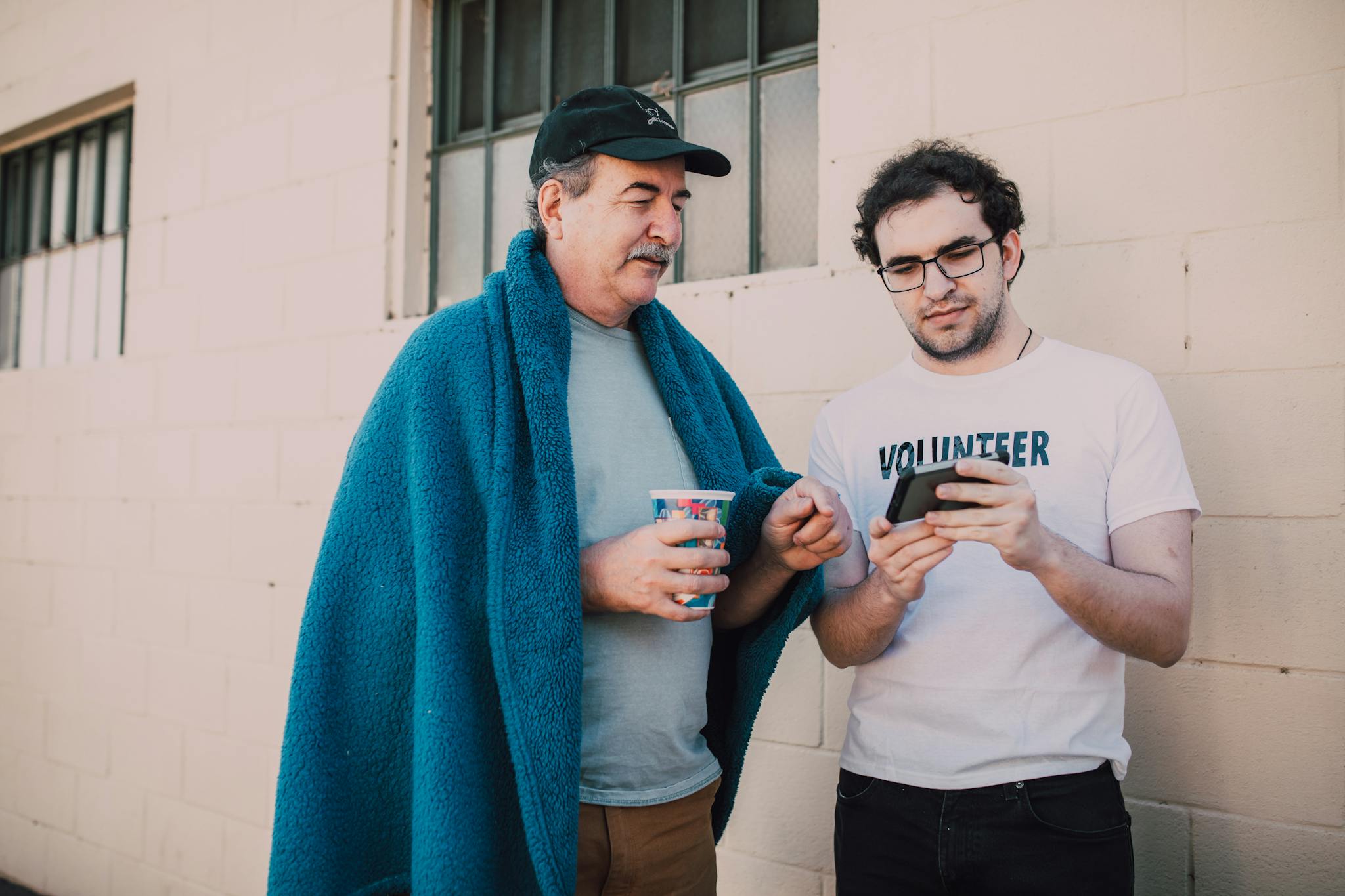 A volunteer helping a homeless man with smartphone services outdoors.