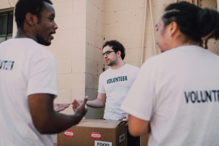 Group of diverse volunteers organizing food donations in white shirts marked with 'Volunteer'.
